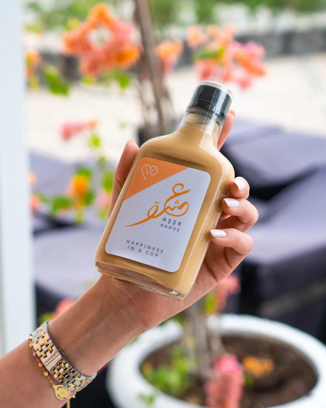 Hand holding a bottled drink in front of pink bougainvillea