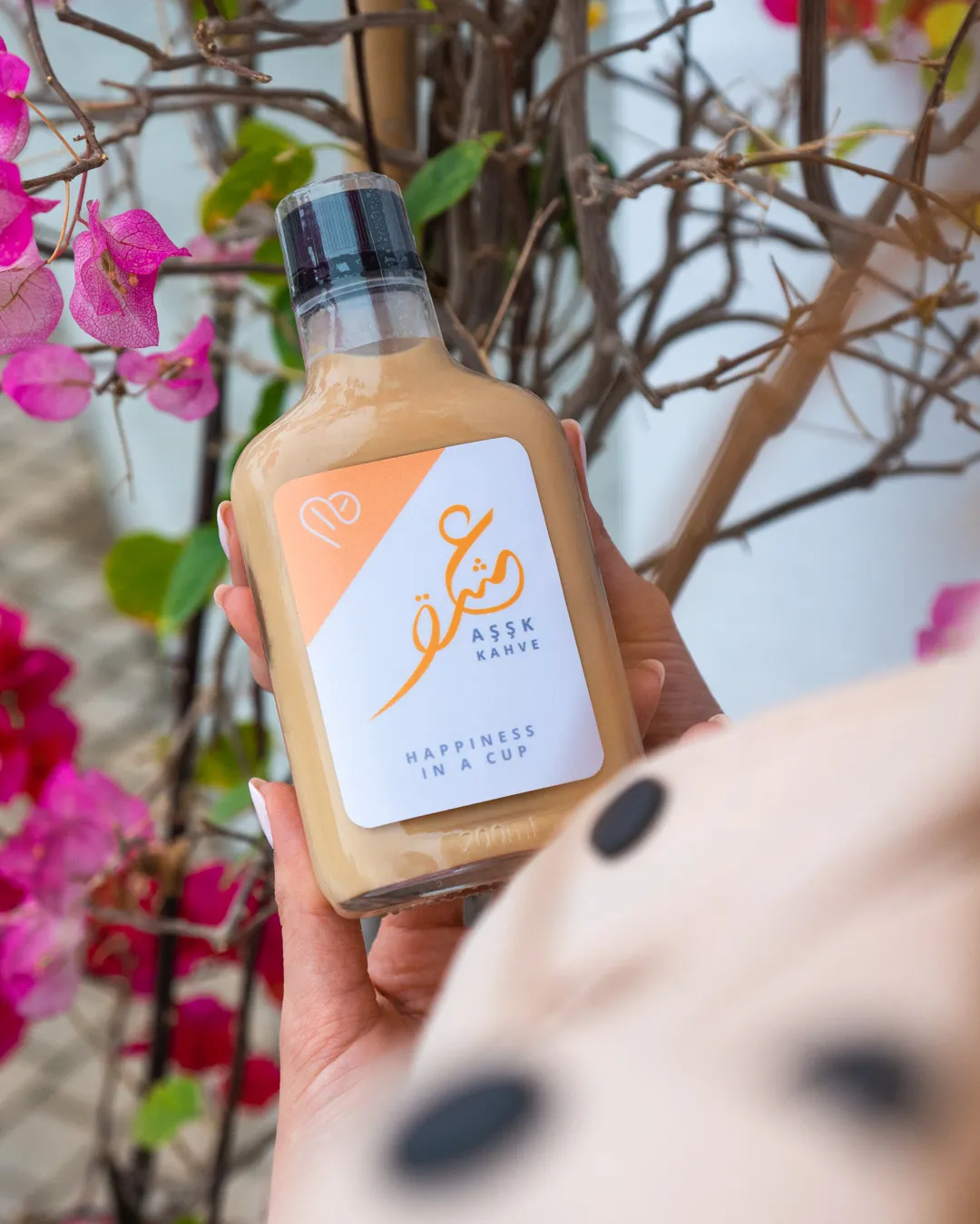 Hand holding a bottled drink in front of pink bougainvillea
