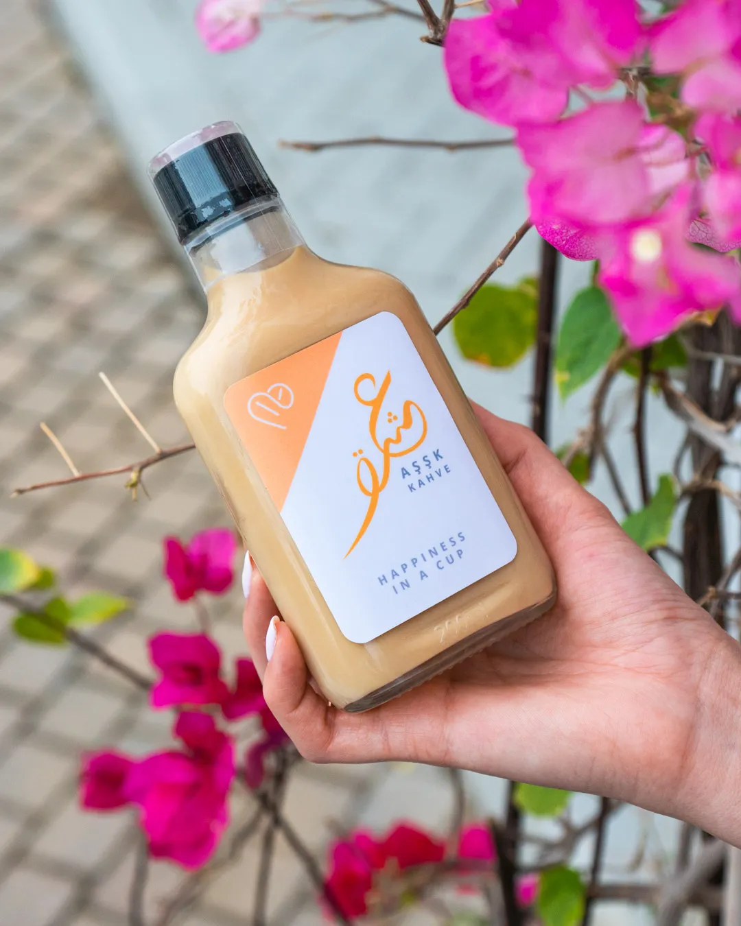 Hand holding a bottled drink in front of pink bougainvillea