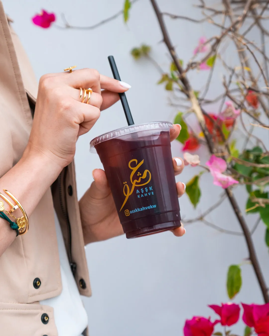 Hand holding a bottled drink in front of pink bougainvillea